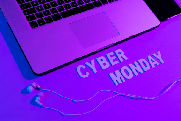 Image of cyber monday text, smartphone, laptop and earphones over neon purple. Retail, savings, online shopping, light and colour concept. - Foto, Imagen