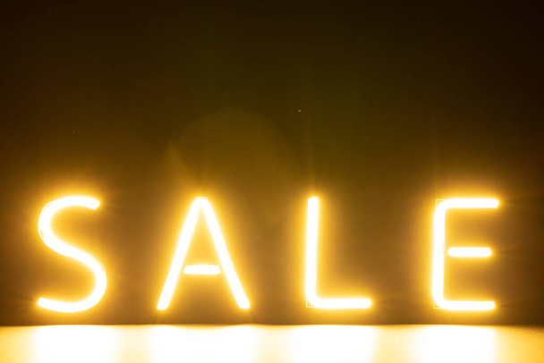Image of glowing neon sale text over orange background. Retail, savings, shopping, light and colour concept. - Foto, afbeelding