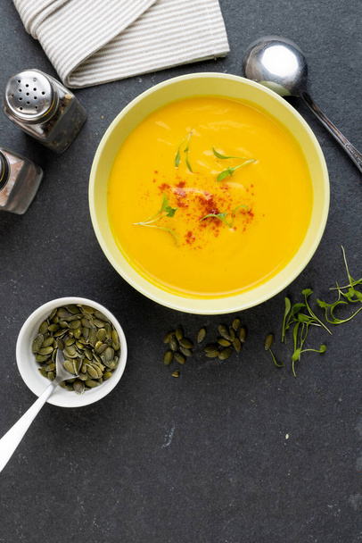 Vertical image of bowl of carrot soup with garnish, and pumpkin seeds on slate, copy space. Tasty home cooked food and healthy eating. - Φωτογραφία, εικόνα