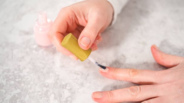Kobieta kończąca manicure w domu prostymi narzędziami do manicure. Malowanie paznokci z lakierem do paznokci. - Zdjęcie, obraz