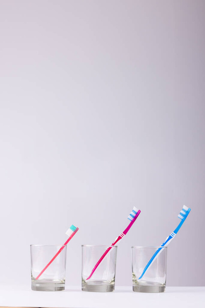 Vertical image of toothbrushes in glasses on grey background. Health, dentistry, dental accessories and taking care of teeth concept. - Valokuva, kuva