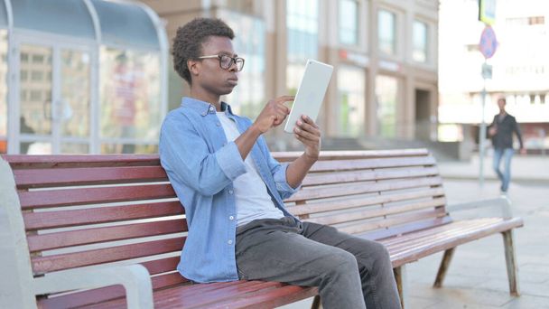 Африканський чоловік користується планшетом, сидячи на вулиці на лаві - Фото, зображення