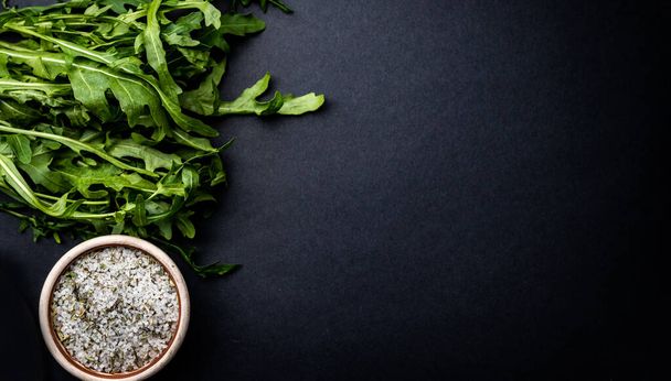Green arugula and salt with herbs on dark grey background with copy space. Healthy food composition of organic vegan nutrition - Valokuva, kuva