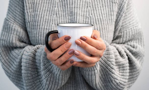 Person holding mug with hot beverage in hands. Girl in sweater with rustic cup in winter time closeup - Foto, Imagen