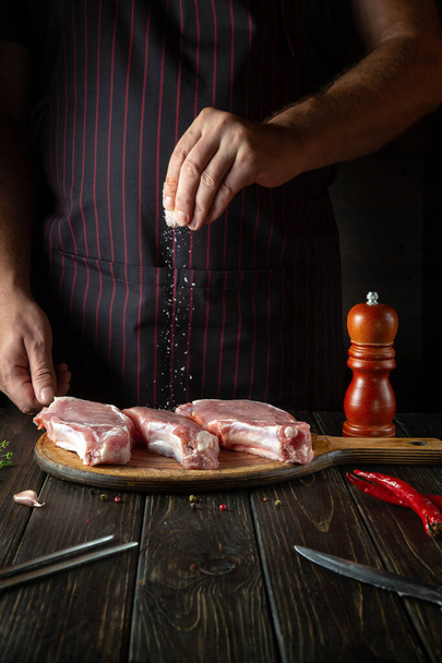 The chef sprinkles raw ribs with salt. The concept of cooking delicious food for the hotel or restaurant. - Foto, imagen