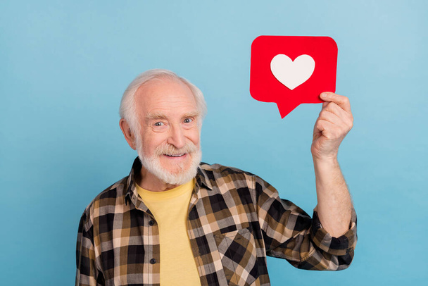 Photo of dreamy pretty man pensioner dressed checkered shirt holding heart like sign isolated blue color background. - Fotoğraf, Görsel