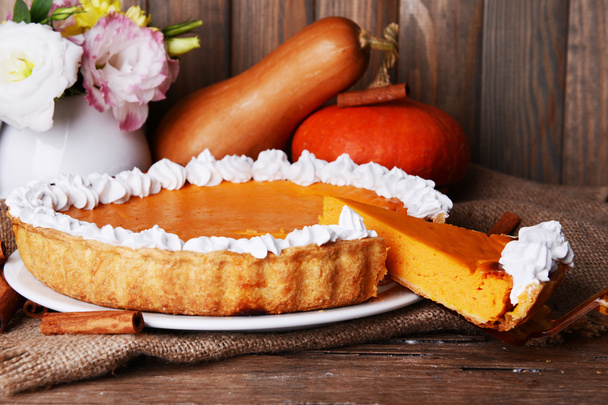 Composition of homemade pumpkin pie on plate and fresh pumpkins on wooden background - Foto, imagen