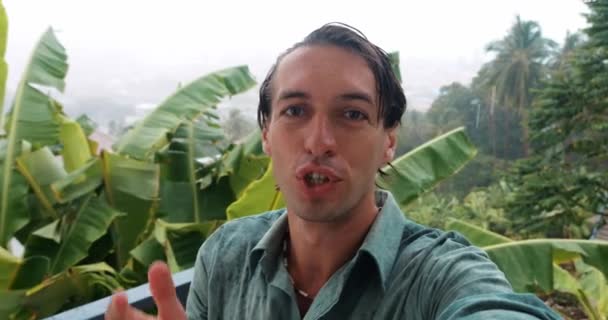 Attractive guy blogger, vlogger records movie for his travel blog, standing wet under tropical rain, in relax at nature - Footage, Video
