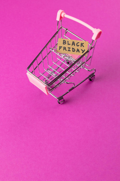 Composition of shopping cart with black friday text on pink background. Retail, shopping and black friday concept. - 写真・画像