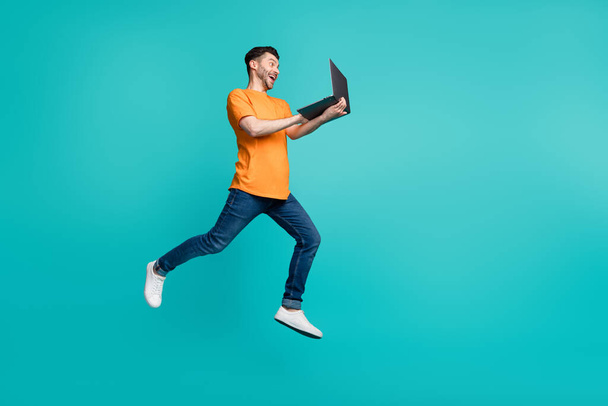 Full length photo of crazy guy jump high work netbook search web sale isolated on cyan color background. - Фото, изображение