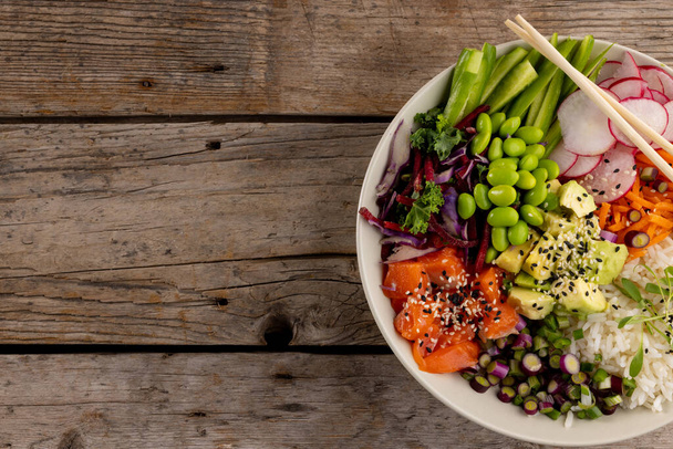 Overhead view of hawaiian poke bowl with chopsticks and copy space on wooden background. Hawaiian tasty fresh food and healthy eating. - Foto, Imagen
