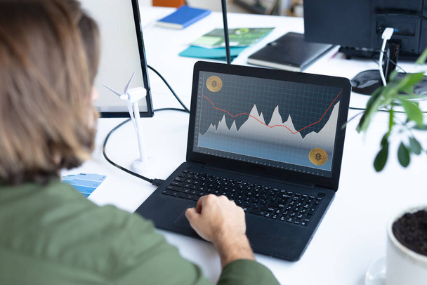 Caucasian businesswoman sitting at desk, using laptop with statistical data on screen. business communication and digital interface technology digital composite image. - Foto, imagen