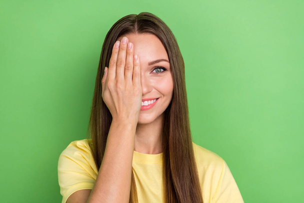 Portrait of nice adorable cute girl with straight hairstyle dressed yellow t-shirt palm cover eye isolated on green color background. - Foto, afbeelding