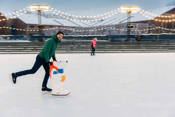 Portret van gelukkig midden leeftijd mannelijke schaatser op ijs ring staat, geniet van vrije tijd, heeft actieve levensstijl, op ijs arena. Lachende blije mens verheugt zich ijzig winterweer. Skate ontwikkelingshulp. Hobby concept - Foto, afbeelding