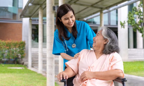 Tekerlekli sandalyedeki hastayla ilgilenen Asyalı dikkatli bir bakıcı ya da hemşire. Bakıcının, birikimin ve sağlık sigortasının özenle mutlu emeklilik kavramı. Mutlu bir aile. - Fotoğraf, Görsel