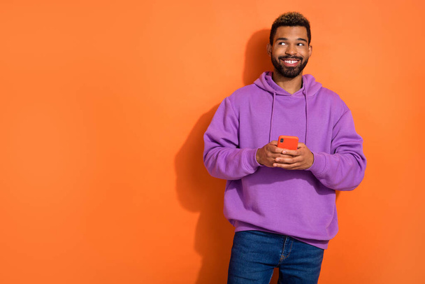 Photo de gars attrayant porter des vêtements violets acheter à rabais appareil moderne regarder espace vide profiter isolé sur fond de couleur orange. - Photo, image