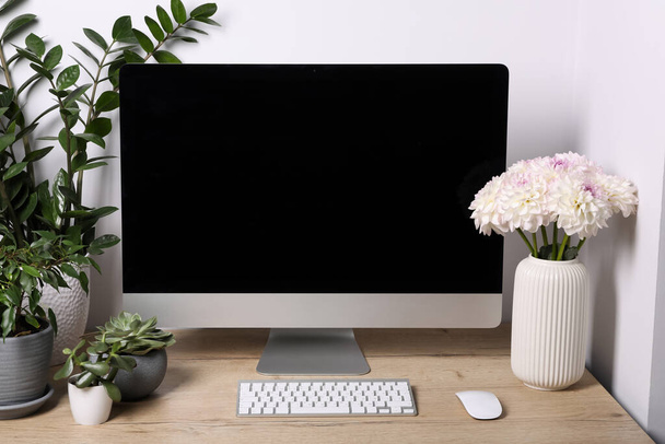 Comfortable workplace with modern computer, green houseplants and beautiful flowers on wooden table indoors - Photo, image