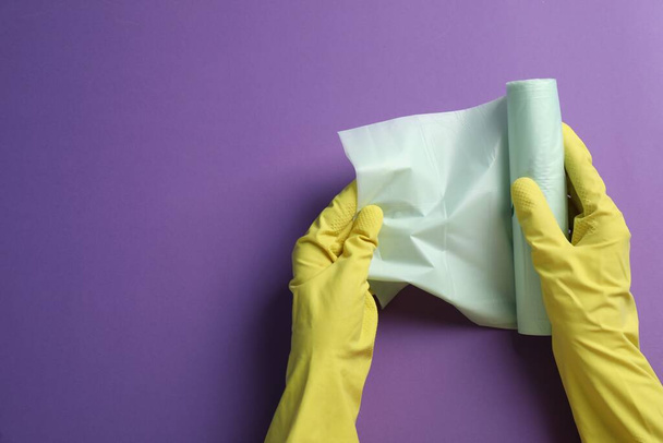 Janitor in rubber gloves holding roll of color garbage bags over purple background, top view. Space for text - Foto, Imagen