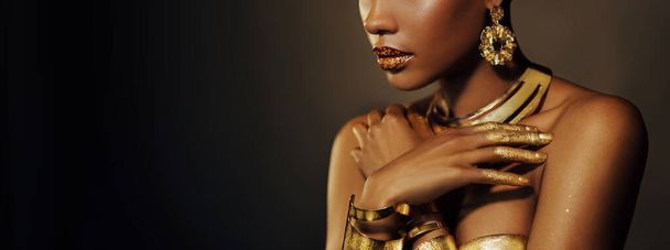 Portrait Closeup shiny golden lip gloss on lips Beauty fantasy African American woman, cropped face in gold paint perfect skin. Fashion model girl goddess. jewellery accessories art metallic makeup - Photo, image