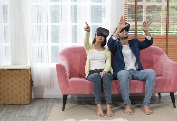νεαρό ζευγάρι που χρησιμοποιεί ακουστικά εικονικής πραγματικότητας παιχνίδι στο σαλόνι στο σπίτι.concept τεχνολογία με οικογενειακό τρόπο ζωής, ψυχαγωγία το Σαββατοκύριακο - Φωτογραφία, εικόνα