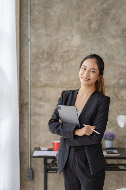 Bizneswoman stojąca z tabletem pracującym obok szklanej ściany w biurze. - Zdjęcie, obraz