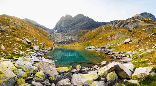 Mountains green lake with reflections and rocky shore in autumn time. Wild nature and rural mount valley. Fall grey weather rainy clouds on sky. Cold lake, winter coming landscape - Foto, afbeelding