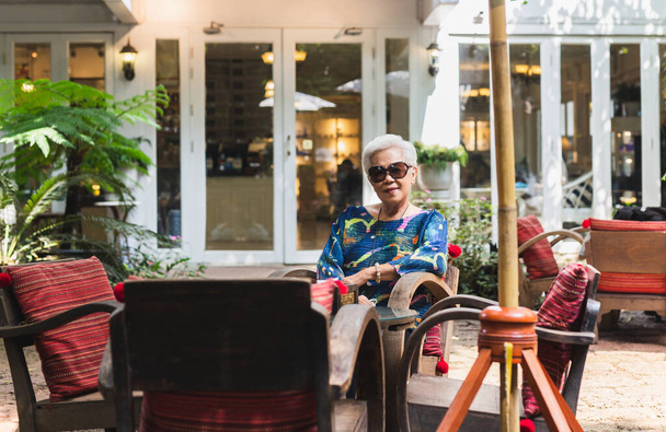 Retrato de mulher sênior em óculos de sol sentado em uma cadeira no café ao ar livre - Foto, Imagem