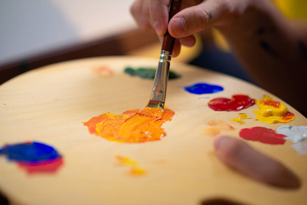A man is using a flat brush to mix two colours on a palette and paint onto a canvas. - Photo, Image