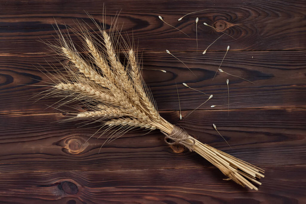 木製のテーブルの上の花束の小麦の耳。木の背景に小麦の葉。収穫の概念. - 写真・画像