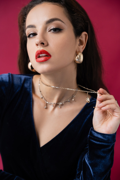 glamour woman with red lips touching necklace and looking at camera isolated on burgundy - Fotografie, Obrázek