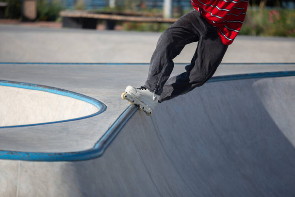 Inline skater doing trick in outdoor skatepark. In-line roller blader performing top acid grind on rail in concrete mini ramp - Foto, Imagem