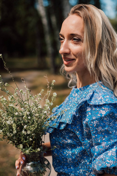 Egy fiatal, gyönyörű nő kék ruhában vadvirágokat tart a kezében. Kiváló minőségű fénykép - Fotó, kép