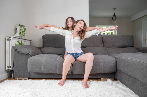 Portrait of playful and excited little boy holding his mother hands while pretending to fly for fun at home. Happy caucasian mother bonding and relaxing with her son. High quality photography - Foto, Bild
