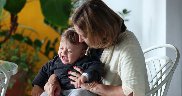 Grandmother holding crying baby grandson. Grand-parent trying to console tearful infant child - Photo, image