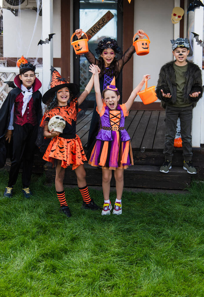 Веселые межрасовые дети празднуют Хэллоуин во время вечеринки на заднем дворе - Фото, изображение
