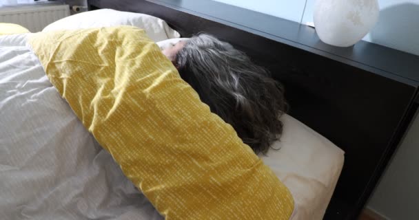 Зрелая женщина мирно спит, переворачивается, не просыпаясь все еще спит, солнечный свет проходит через окно, движется медленно, длинные седые волосы, желтое одеяло, абсолютное спокойствие - Кадры, видео