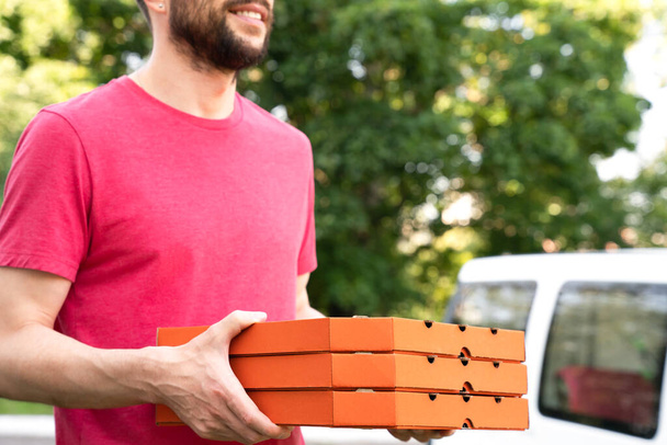 屋外でピザボックスを持っている若い男を笑顔。ピザの配達だ。選択的焦点. - 写真・画像