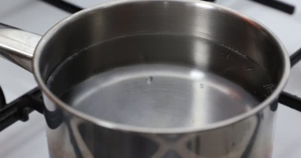 Primer plano del agua limpia y transparente que comienza el proceso de ebullición, pequeñas burbujas, parrilla negra, estufa blanca, bandeja de metal. Concepto de comida casera - Imágenes, Vídeo