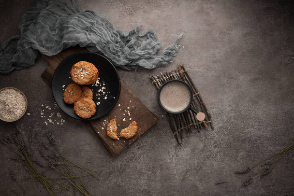 Homemade oatmeal raisin cookies with cup of cappuccino on rustic background. - 写真・画像