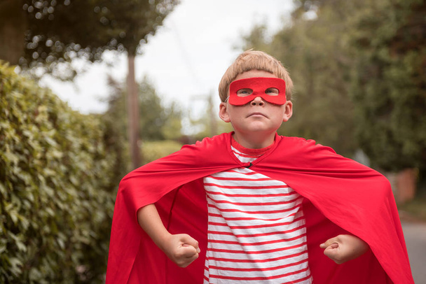 Funny kid wearing super hero costume ready to educate. Boy with funny face go to change the world. Celebrating surprised and amazed for success with strong arms. Hero school. - Photo, image