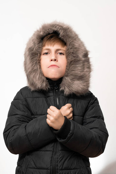 A boy in a winter jacket with a hood on a white background, showed the aggression of a child in emotions. - Foto, Imagen