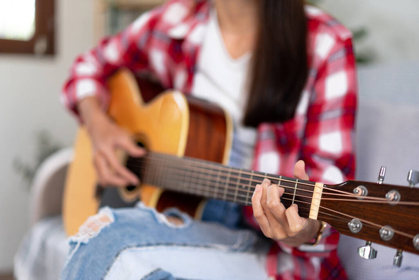 Mujer joven es la práctica de acordes básicos de guitarra y tocar la guitarra con canciones pop mientras está sentado en el cómodo sofá en la sala de estar en casa. - Foto, imagen
