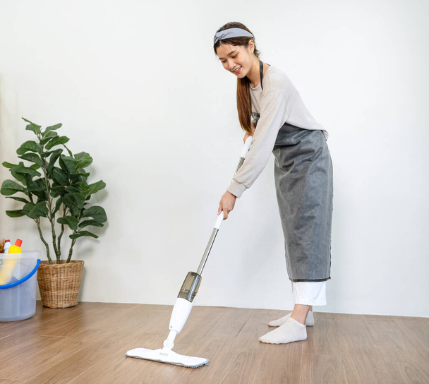 Housekeeper é usar esfregona com aspirador de pó para limpeza com aspiração e limpeza laminado sujo no chão na sala de estar, enquanto trabalhava para realizar a limpeza da casa de rotina. - Foto, Imagem