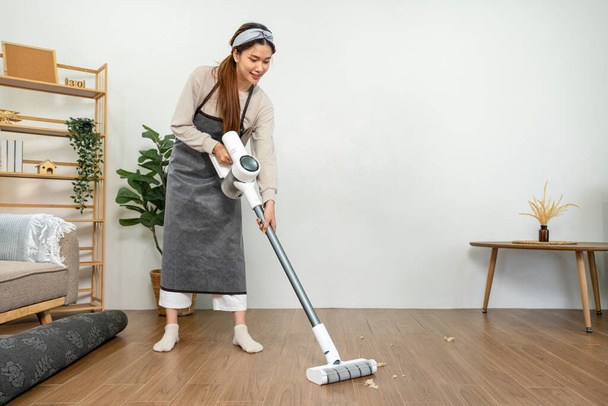 Housekeeper is use mop with vacuum cleaner to housekeeping with vacuuming and wiping dirty laminate on the floor in living room while working to perform routine house cleaning. - Foto, immagini