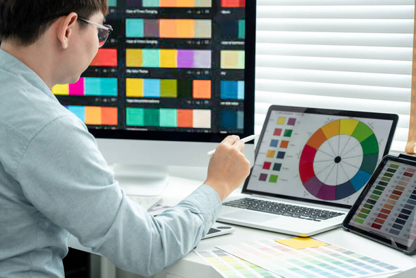 Male graphic designer is choosing color swatch samples on multiple screens and sketching on tablet digital to working graphic design with technology in modern office. - Foto, immagini