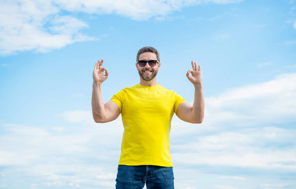 happy man in yellow shirt and sunglasses on sky background. ok. - Photo, Image