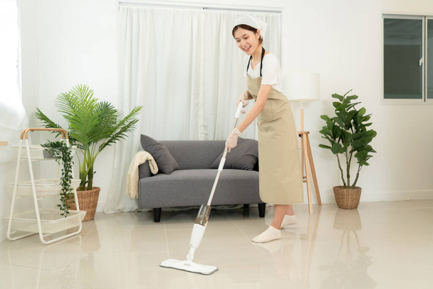 A házvezetőnő porszívós felmosót használ a takarításhoz, porszívózással és piszkos laminát törléssel a nappaliban a padlón, miközben a rutin takarítás elvégzésén dolgozik.. - Fotó, kép