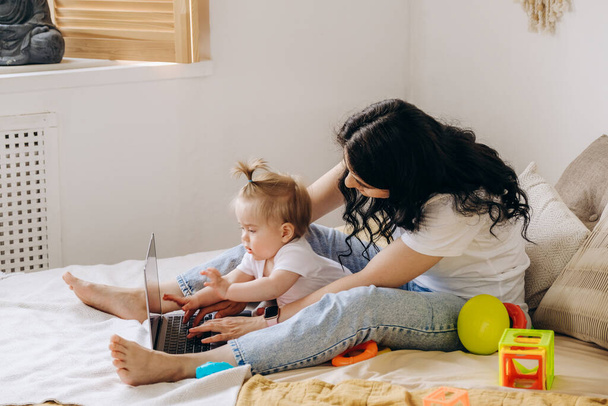Freelancer woman working at home. The kid prevents his mother from working on the laptop on the Internet. Remote work. Work online. The baby does not allow the mother to work at home. - Photo, Image