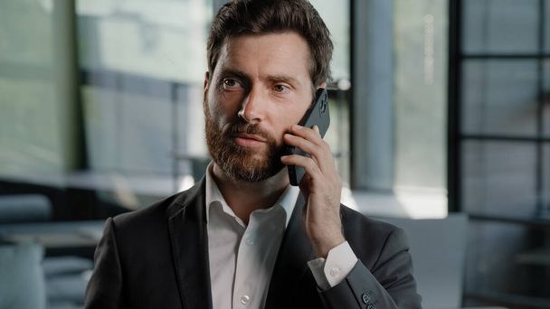 Γενειοφόρος Καυκάσιος μεσήλικας επιχειρηματίας που μιλάει στο τηλέφωνο στο γραφείο εξηγεί διαπραγματεύονται εικονικές πωλήσεις συνομιλία χρησιμοποιώντας κινητό αρσενικό επαγγελματική επικοινωνία ομιλίας με κινητό τηλέφωνο chat - Φωτογραφία, εικόνα