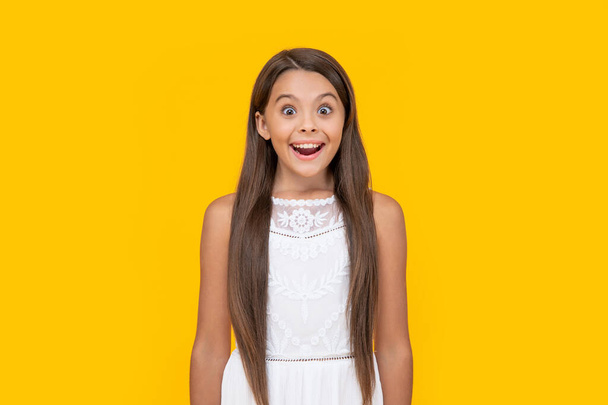 amazed teen girl in white dress has long hair on yellow background. - Foto, Imagen